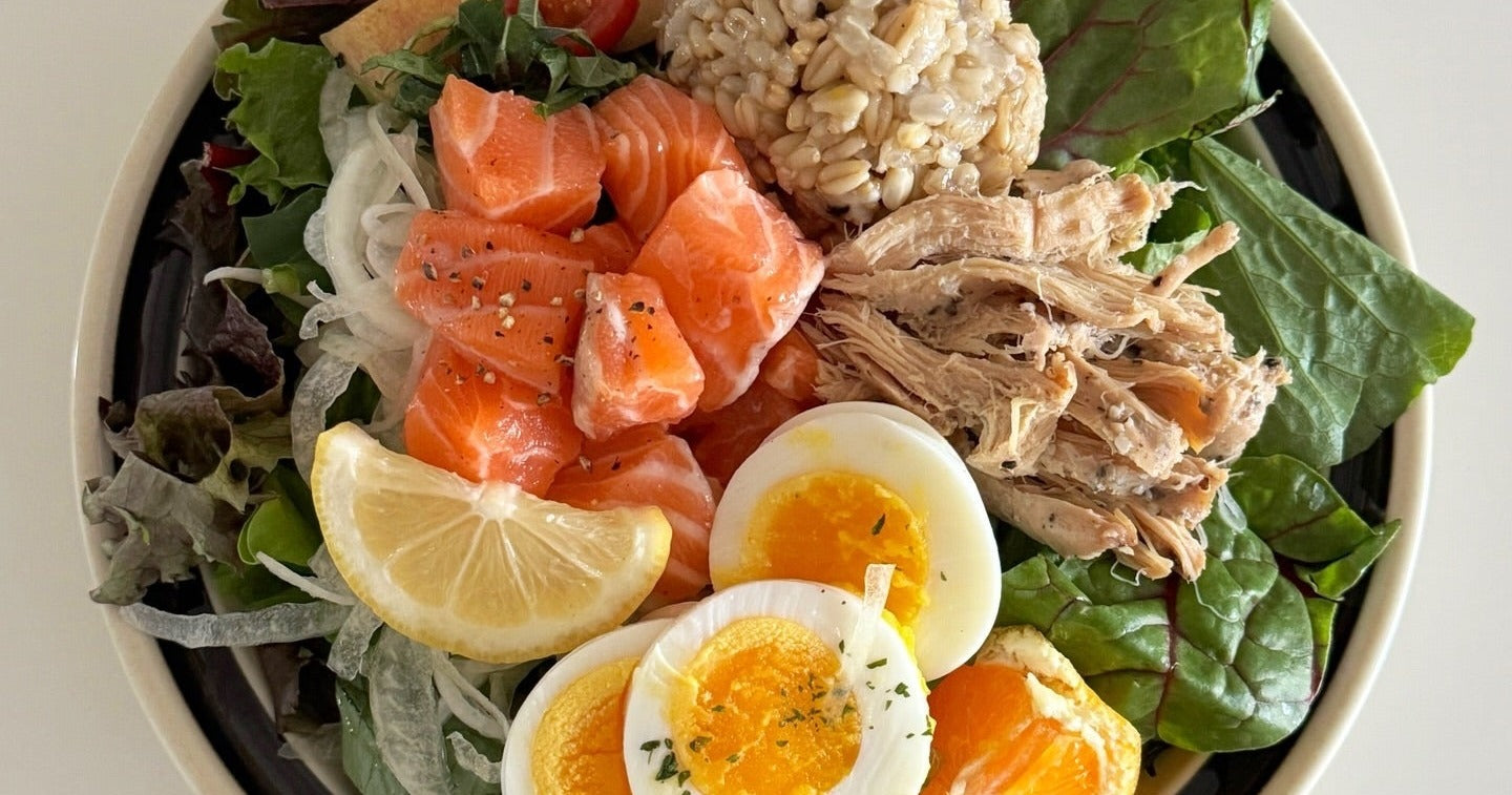 High-protein lunch bowl with shredded chicken breast, salmon, boiled eggs and greens