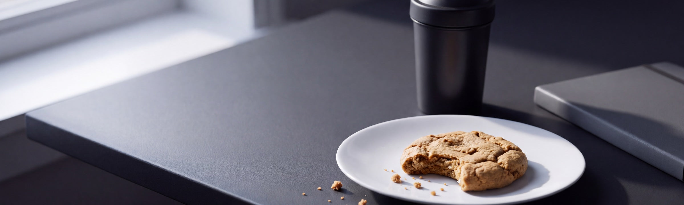 A protein cookie on a desk with a shaker behind it